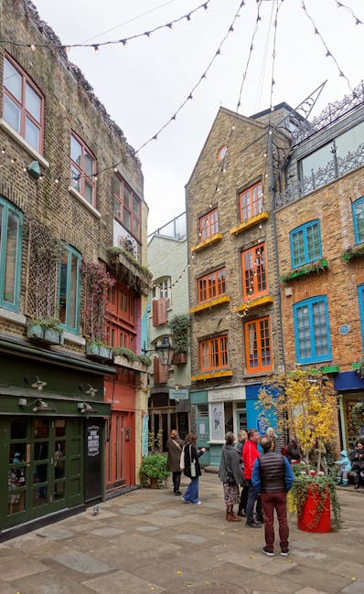 The image depicts a vibrant cobblestone outdoor courtyard surrounded by colorful, multi-story buildings with distinctive window frames painted in shades of blue, orange, green, and red. String lights 