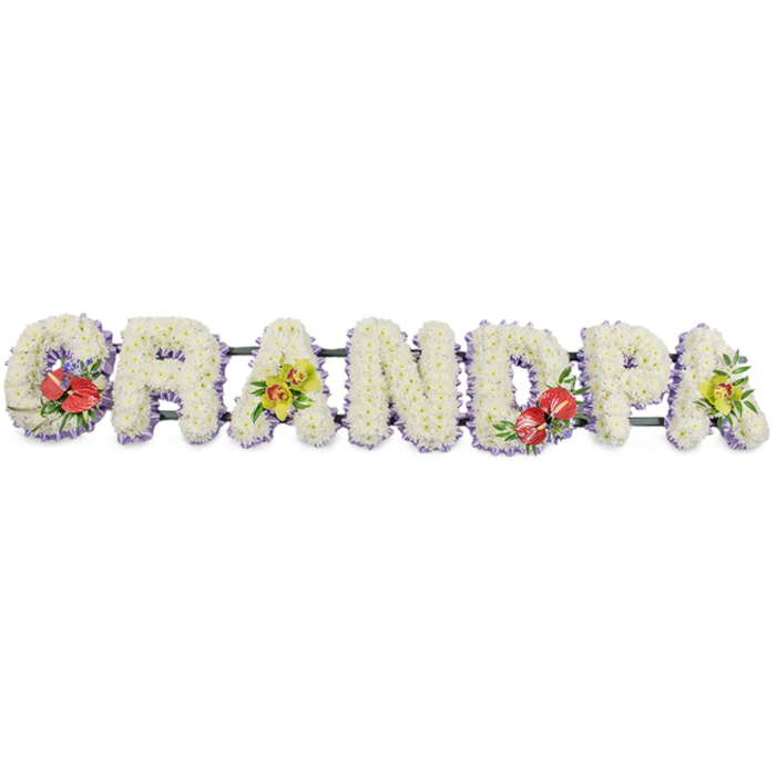 A personalised funeral flower tribute stretches horizontally across the frame, spelling out "GRANDPA" in solid capital letters that immediately draw the eye. The entire arrangement sits against a bright white background, which enhances the crisp clarity of the design and lets the flowers themselves tell the story. Each individual letter is built from a dense bed of pure white chrysanthemums, packed tightly together so their small, daisy-like heads merge into a single, plush surface. This soft texture suggests comfort and serenity, making the tribute especially fitting for a final farewell to a beloved grandfather. Along the base of each letter, a fine edging of pale lavender ribbon peeks through the blooms, providing a delicate halo of colour that gently separates the letters from the background, much like the subtle artistry often showcased by Covent Garden florists preparing flowers for nearby churches and theatres. The letters are supported from behind by dark green bars, ensuring the name stays perfectly aligned when placed beside the coffin, on a hearse, or at the front of a memorial service. Four prominent floral sprays add richer tones and emotional detail. On the "G" and "D," deep red anthuriums stand proudly, their glossy, heart-shaped spathes and bright yellow spadices offering a symbol of devotion and enduring love, framed by lush green leaves and a hint of purple accent blooms. The first "A" and the final "A" are softened with clusters of yellow-green orchids, their graceful petals and fresh colour bringing a note of hope and warmth. The tribute feels both classic and deeply personal, ideal for families across Covent Garden who wish to spell out a cherished name in flowers.